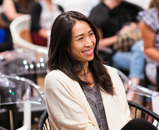 A woman sat in a white jacket sat in an audience smiling