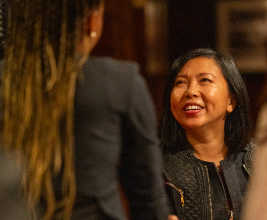 Two women in black jackets engaged in conversation, one facing towards the camera and the other facing away