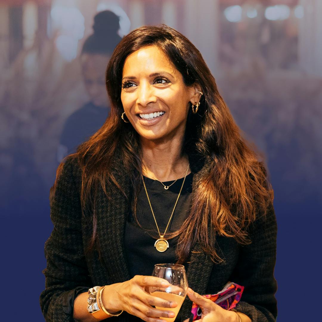 A smiling woman with long brown hair over a black jacket, holding a glass of wine